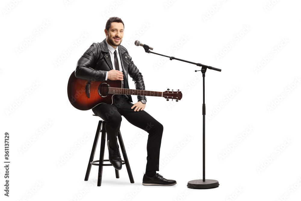 Male singer with an acoustic guitar sitting on a chair with a microphone Male singer with an acoustic guitar sitting on a chair with a microphone