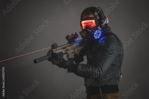 Futuristic soldier in led light helmet with a rifle on dark background.