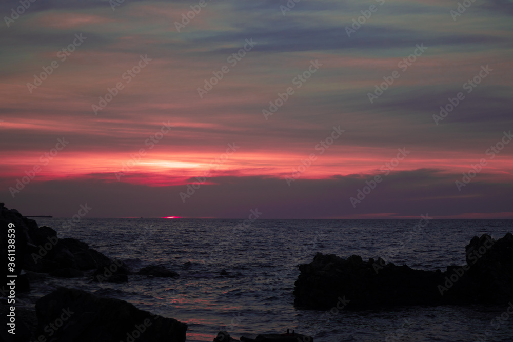colorful pink sunset on rocky beach with cloudy sky