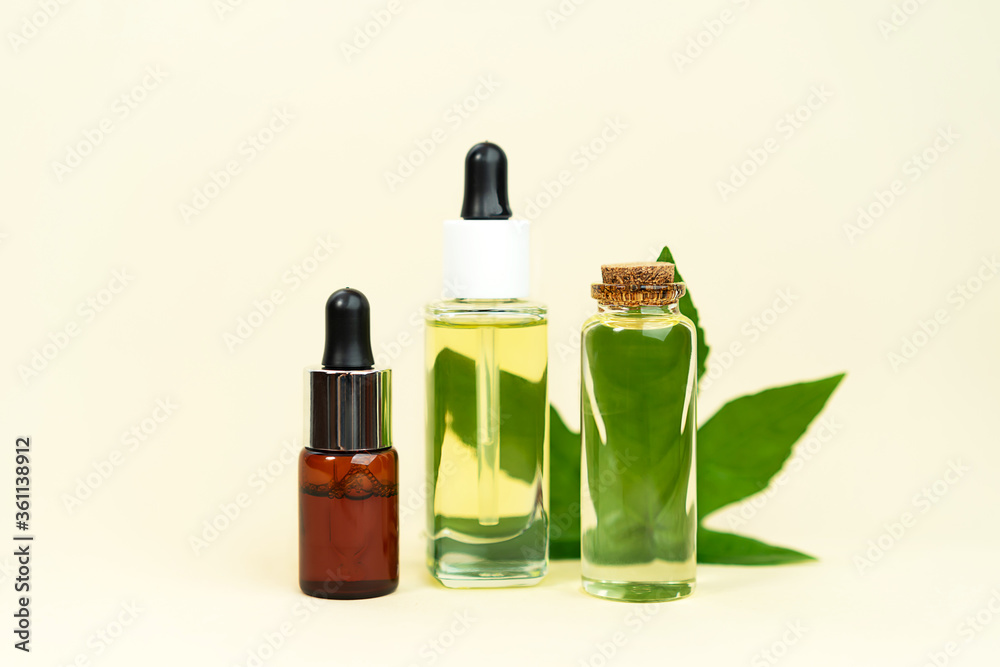 Glass bottles with herbal CBD oil, THC tincture and hemp leaf on pastel beige background. Glass bottles with herbal CBD oil, THC tincture and hemp leaf on pastel beige background.
