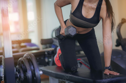 Young woman with sweat doing exercises, working out with dumbbell in fitness gym. Strong and healthy concept. Selected focus.
