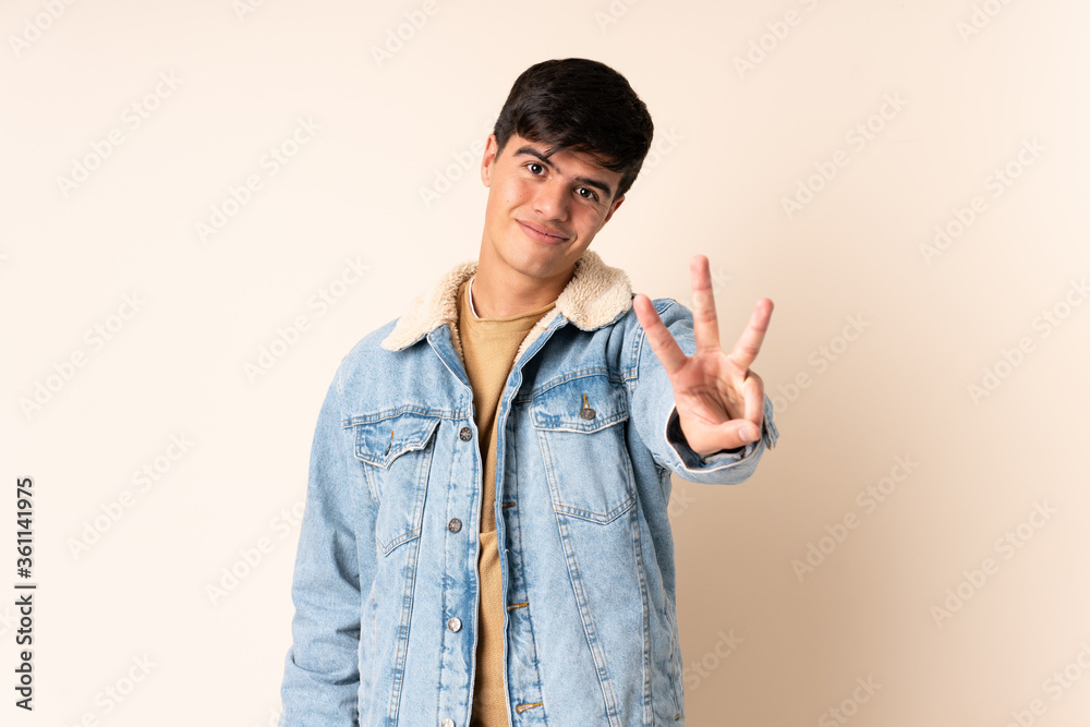 Handsome man over isolated beige background happy and counting three with fingers Handsome man over isolated beige background happy and counting three with fingers