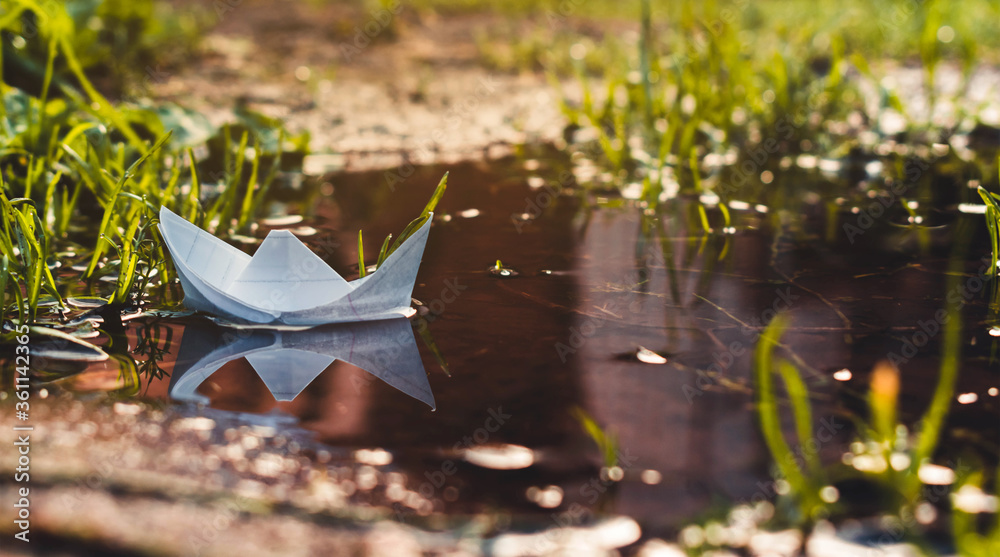 Naklejka premium paisaje en miniatura de un barco de papel sobre una charca de agua, rayos de sol y reflejos en el agua del barco 