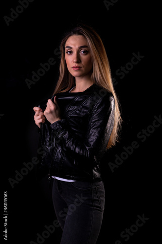 A young girl in a black leather jacket isolated on a black background