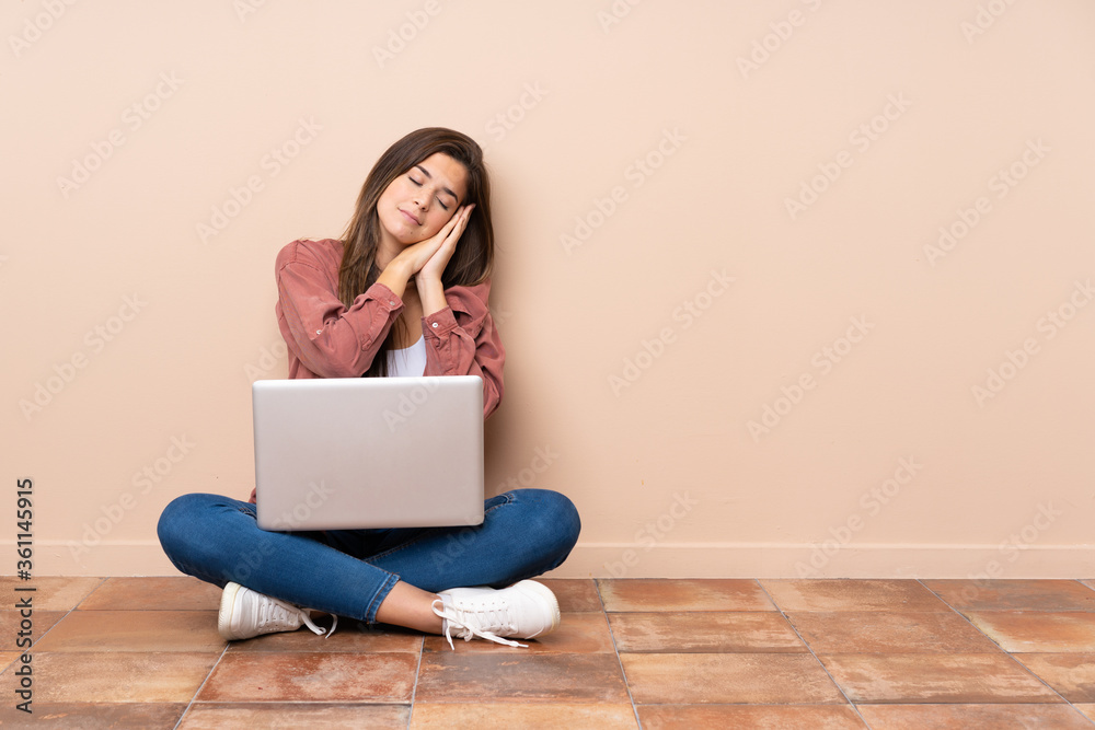 Teenager student girl sitting on the floor with a laptop making sleep gesture in dorable expression Teenager student girl sitting on the floor with a laptop making sleep gesture in dorable expression