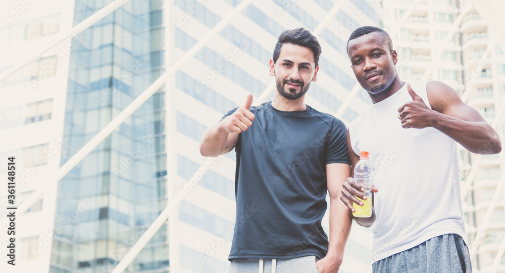 Naklejka premium Happy two handsome muscular athletes stand and showing thumb up with city background.