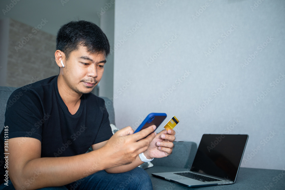 Asian man is holding credit card and using smart phone shopping online at home.Online shopping, e-commerce, internet banking, spending money, working from home concept Asian man is holding credit card and using smart phone shopping online at home.Online shopping, e-commerce, internet banking, spending money, working from home concept