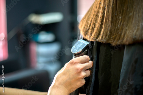 Hairdresser makes haircut to a girl in with long blonde hair. Hairdresser hands holding.