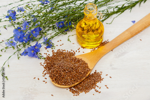 Flax seeds and a a bottle of flaxseed oil on a wooden background. Healthy food and drink concept. Flax seeds is a superfood. Blue flower of flax 