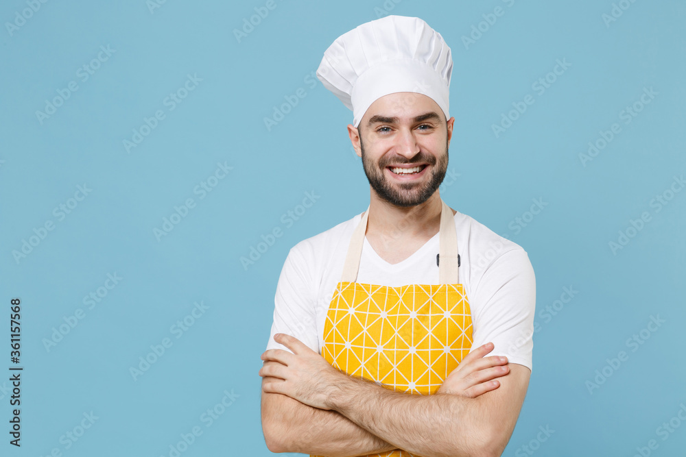 Smiling young bearded male chef or cook baker man in apron white t-shirt toque chefs hat isolated on pastel blue background studio. Cooking food concept. Mock up copy space. Holding hands crossed. Smiling young bearded male chef or cook baker man in apron white t-shirt toque chefs hat isolated on pastel blue background studio. Cooking food concept. Mock up copy space. Holding hands crossed.