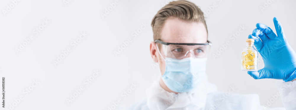 Researcher is testing some vitamins and nutrition drug , wearing mask and PPE and lab glasses Researcher is testing some vitamins and nutrition drug , wearing mask and PPE and lab glasses