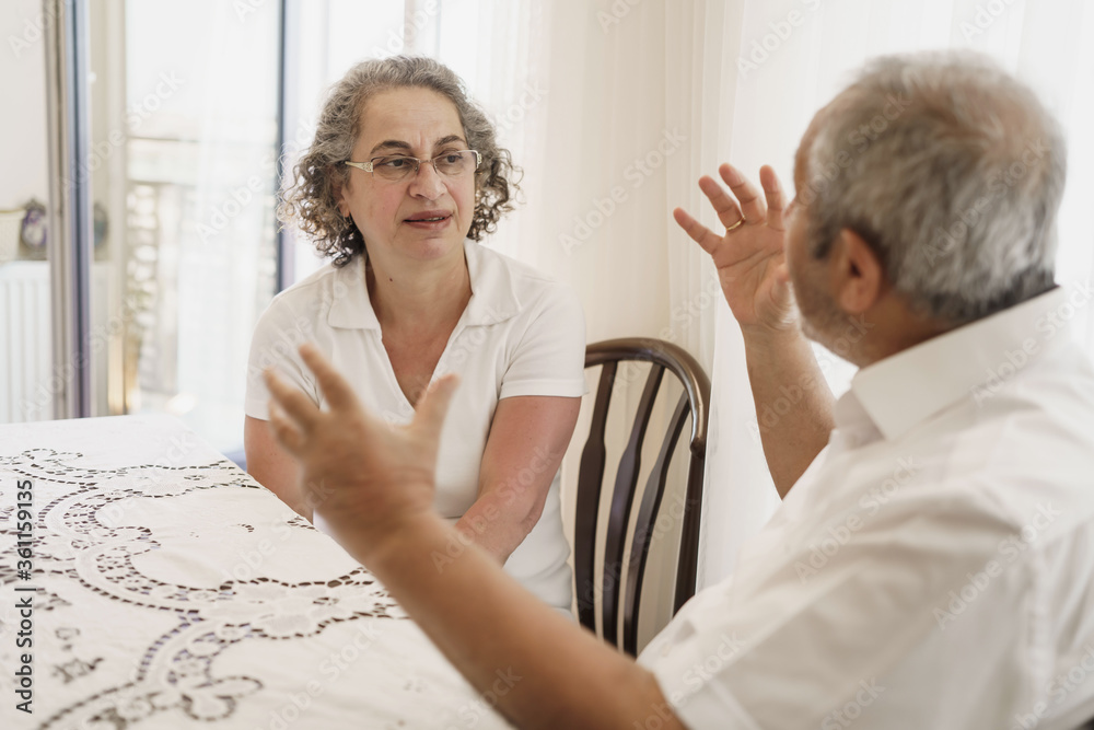 Obraz premium Happy elderly couple, quarantined, sitting alone at home, chatting and laughing.