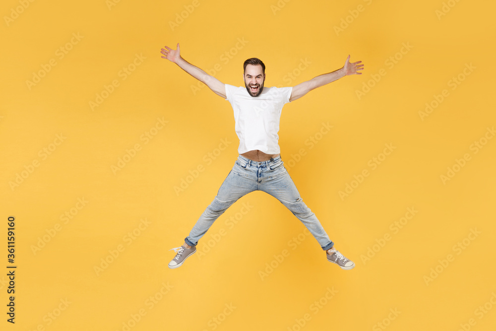 Cheerful young bearded man guy in white casual t-shirt posing isolated on yellow background studio portrait. People emotions lifestyle concept. Mock up copy space. Jumping spreading hands and legs.