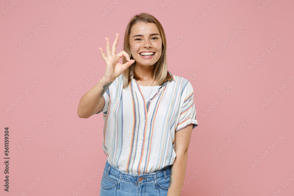 Funny young blonde woman girl in casual striped shirt posing isolated on pastel pink wall background studio portrait. People sincere emotions lifestyle concept. Mock up copy space. Showing OK gesture. Funny young blonde woman girl in casual striped shirt posing isolated on pastel pink wall background studio portrait. People sincere emotions lifestyle concept. Mock up copy space. Showing OK gesture.