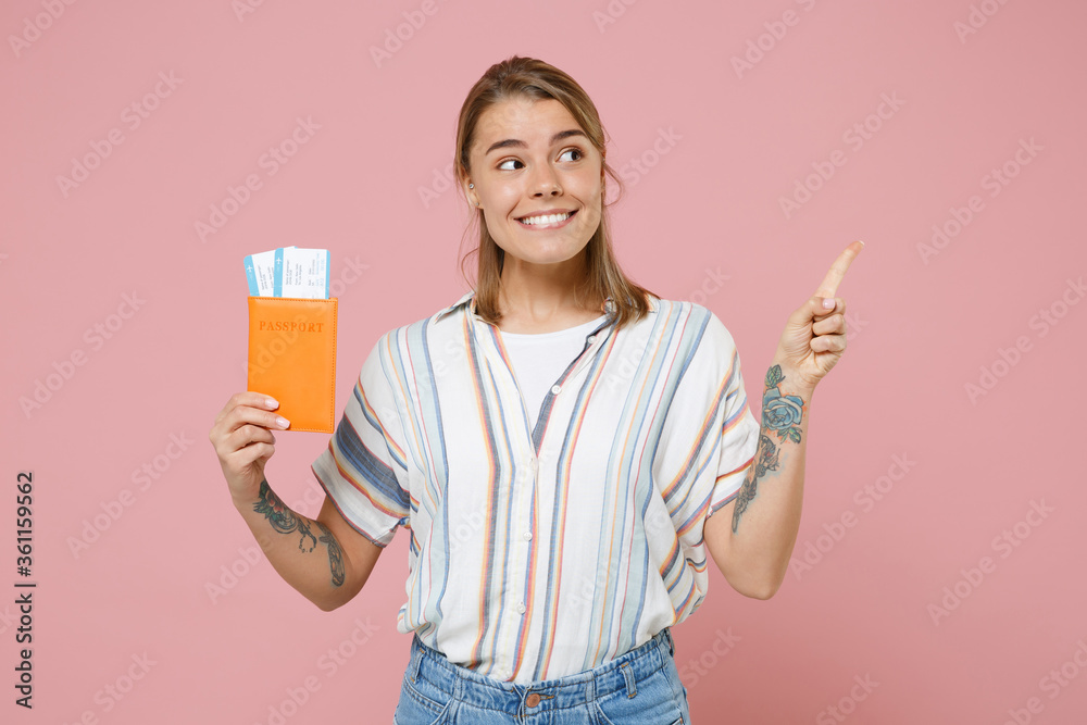 Smiling girl in striped shirt isolated on pink background. Passenger traveling abroad to travel on weekends getaway. Air flight journey concept. Hold passport ticket pointing index finger aside up. Smiling girl in striped shirt isolated on pink background. Passenger traveling abroad to travel on weekends getaway. Air flight journey concept. Hold passport ticket pointing index finger aside up.