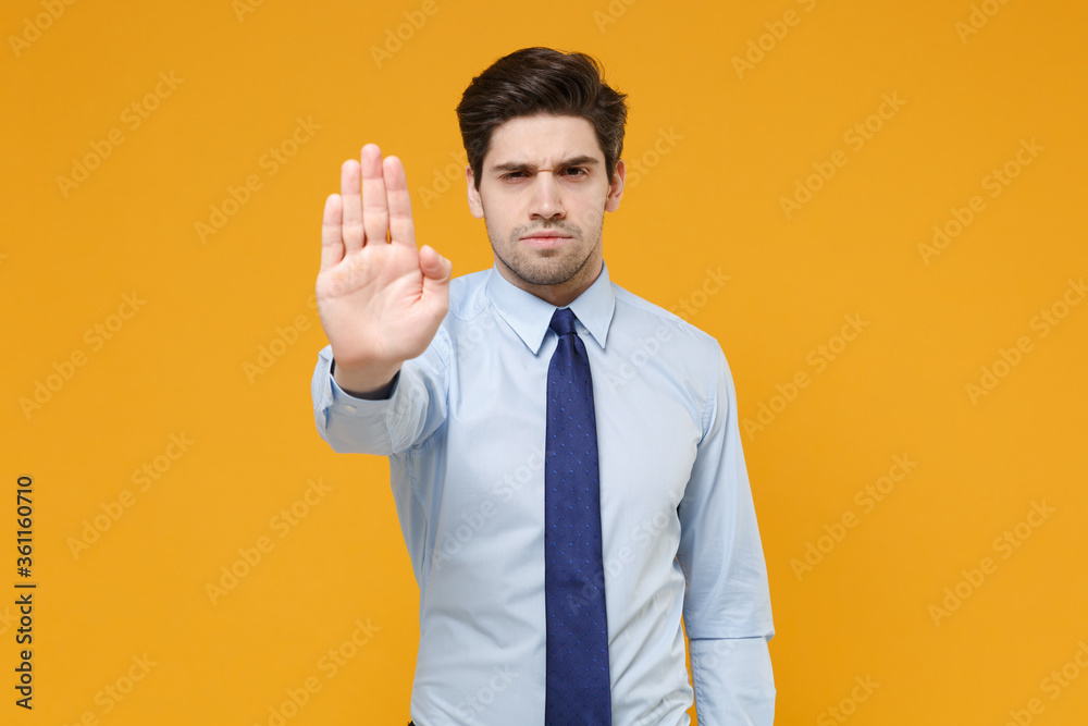 Concerned young business man in classic blue shirt tie posing isolated on yellow wall background studio. Achievement career wealth business concept. Mock up copy space. Showing stop gesture with palm. Concerned young business man in classic blue shirt tie posing isolated on yellow wall background studio. Achievement career wealth business concept. Mock up copy space. Showing stop gesture with palm.