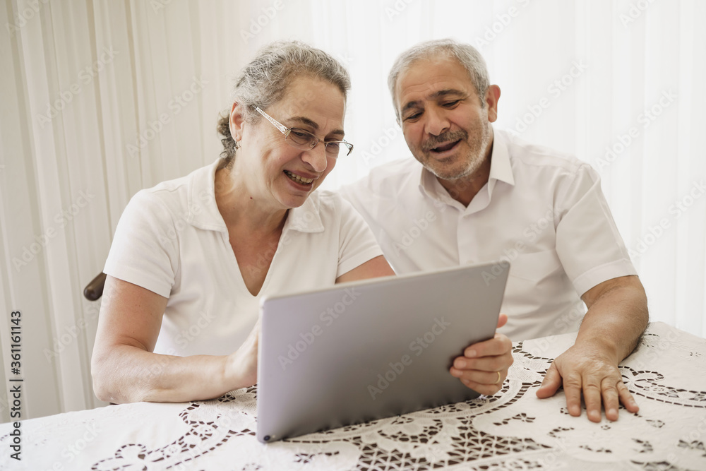 Happy senior couple wave having video call on laptop talking with relatives, smiling aged husband and wife sit on chair at home communicating via online using computer. Elderly and technology concept Happy senior couple wave having video call on laptop talking with relatives, smiling aged husband and wife sit on chair at home communicating via online using computer. Elderly and technology concept