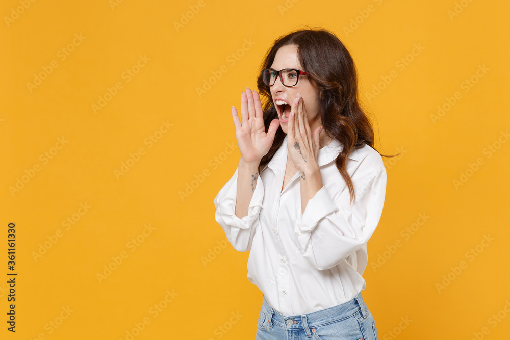 Angry young brunette business woman in white shirt glasses isolated on yellow background studio. Achievement career wealth business concept. Mock up copy space. Scream with hands gesture near mouth. Angry young brunette business woman in white shirt glasses isolated on yellow background studio. Achievement career wealth business concept. Mock up copy space. Scream with hands gesture near mouth.