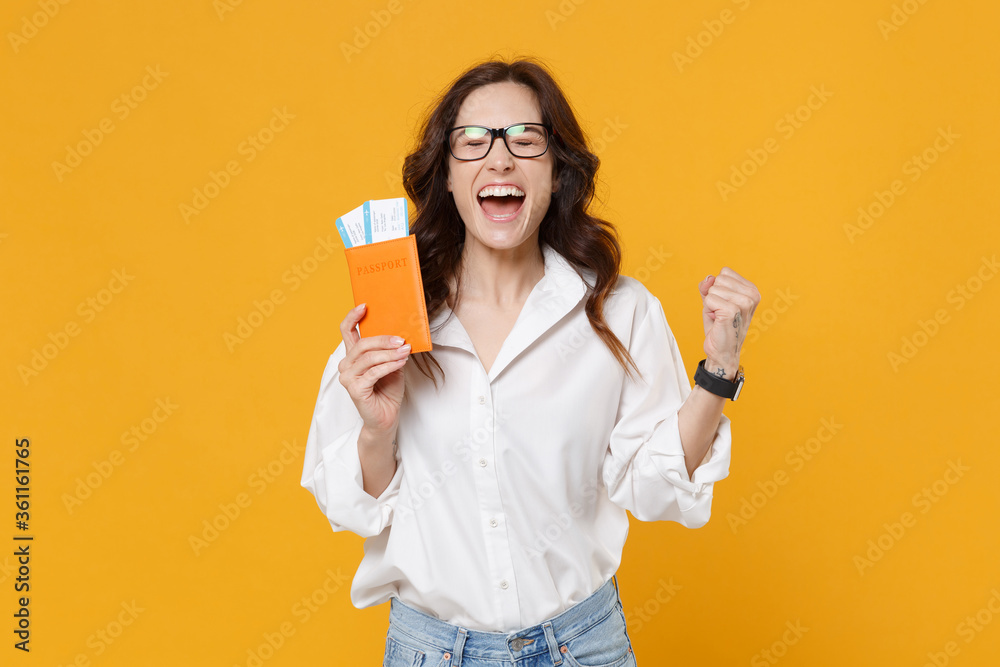 Happy young brunette business woman in white shirt glasses isolated on yellow background. Achievement career wealth business concept. Mock up copy space. Hold passport tickets, doing winner gesture. Happy young brunette business woman in white shirt glasses isolated on yellow background. Achievement career wealth business concept. Mock up copy space. Hold passport tickets, doing winner gesture.
