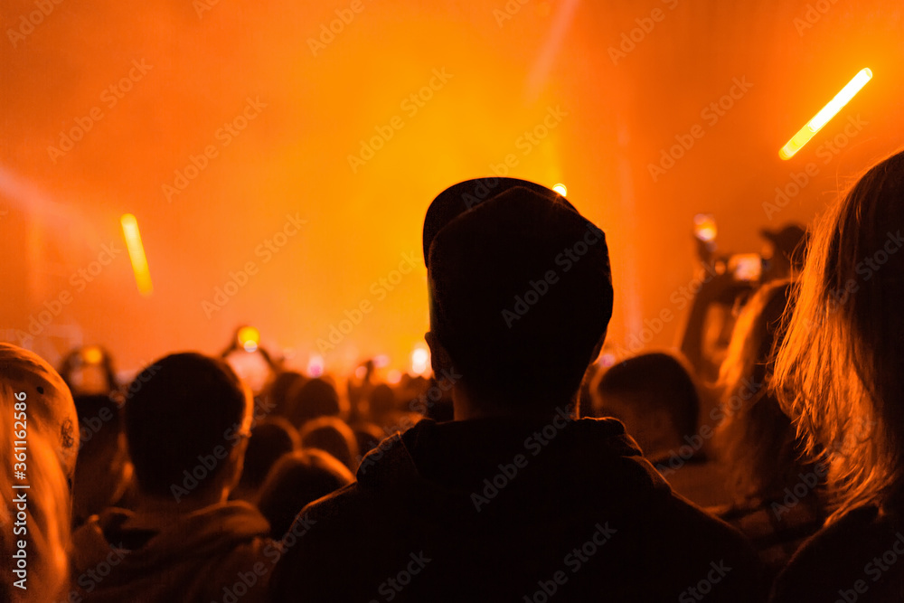A crowd of people at the concert have fun and dance to the music at the concert. Orange light in the background. Rear view. The concept of entertainment and relaxation