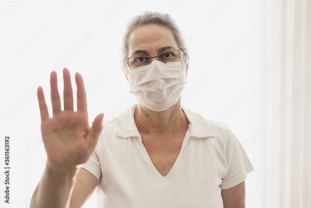 Isolated shot of old woman wearing mask showing stop sign with his open palm, saying that you better stay away from her. keeping hands in stop gesture, saying Stay away from me. Isolated shot of old woman wearing mask showing stop sign with his open palm, saying that you better stay away from her. keeping hands in stop gesture, saying Stay away from me.