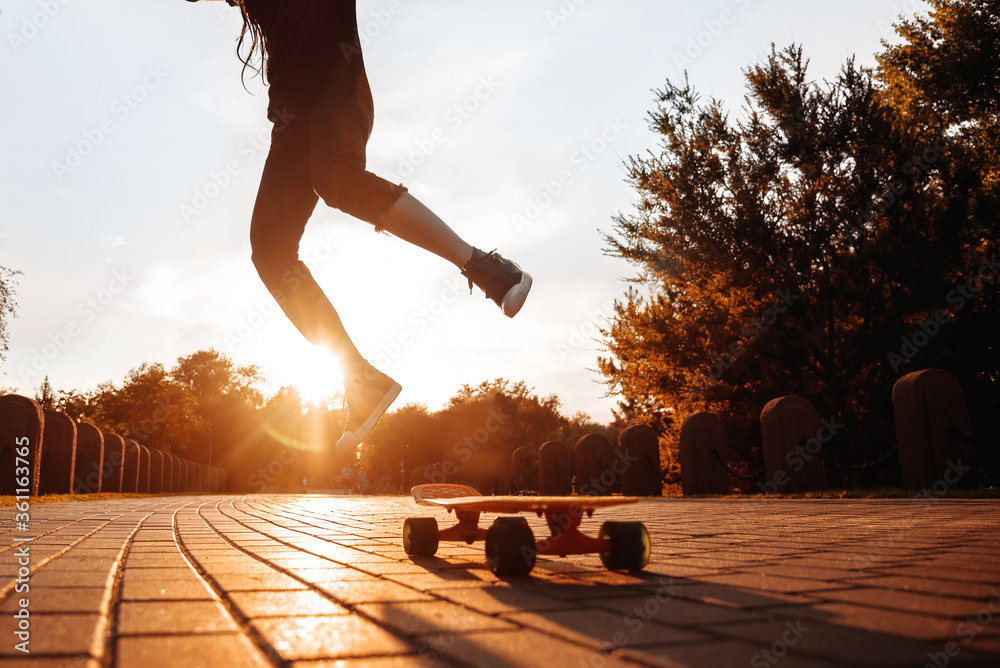 silhouette of a jumping girl on a skateboard in the setting sun in the park