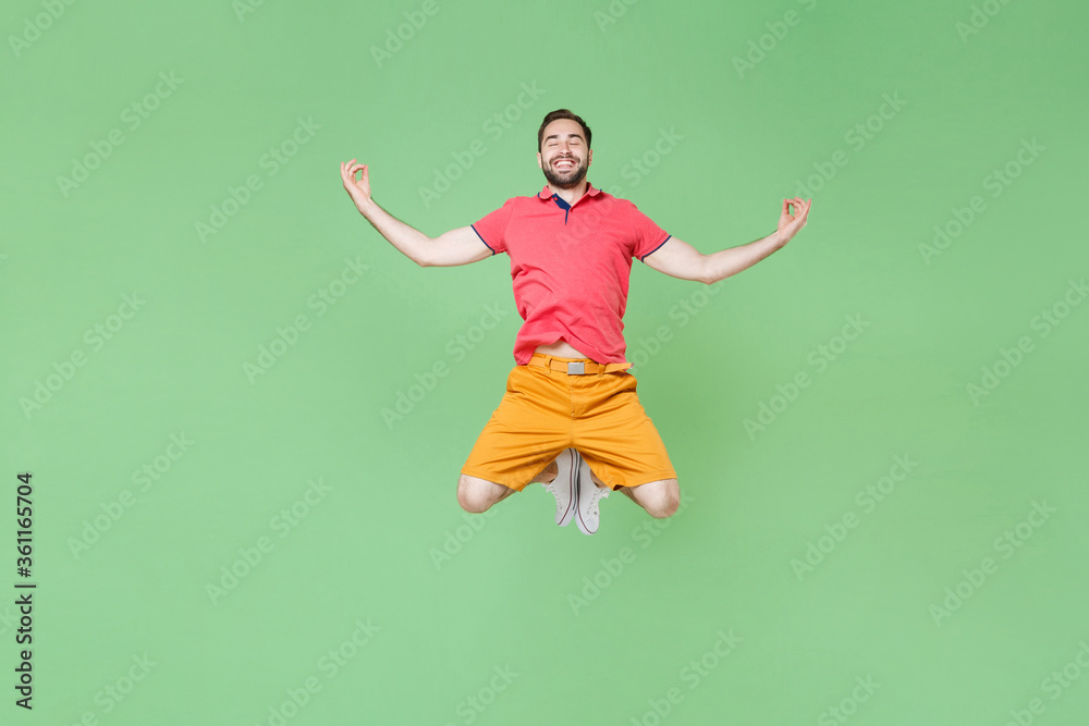 Smiling young bearded man guy in casual red pink t-shirt posing isolated on green background studio portrait. People emotions lifestyle concept. Mock up copy space. Jumping hold hands in yoga gesture. Smiling young bearded man guy in casual red pink t-shirt posing isolated on green background studio portrait. People emotions lifestyle concept. Mock up copy space. Jumping hold hands in yoga gesture.