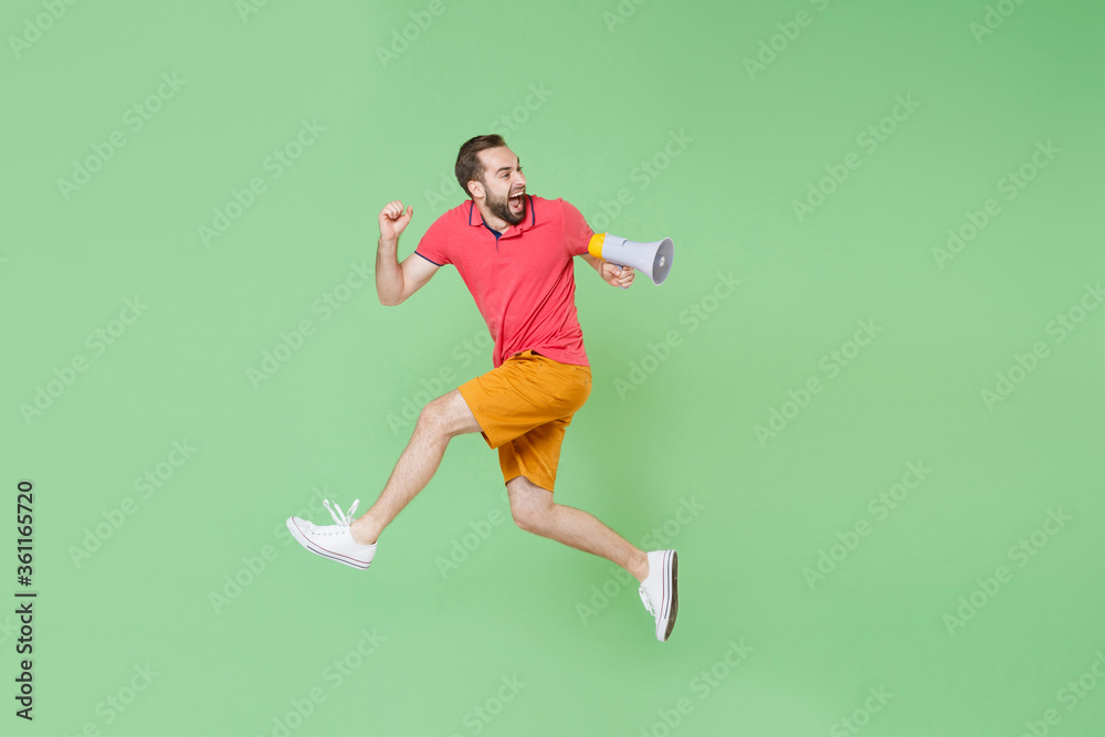 Crazy young bearded man guy in casual red pink t-shirt posing isolated on green background studio portrait. People lifestyle concept. Mock up copy space. Jumping like running, scream in megaphone. Crazy young bearded man guy in casual red pink t-shirt posing isolated on green background studio portrait. People lifestyle concept. Mock up copy space. Jumping like running, scream in megaphone.