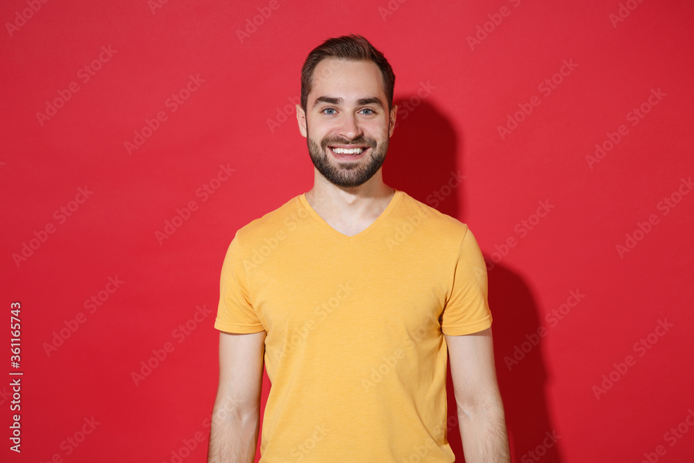 Smiling handsome young bearded man guy in casual yellow t-shirt posing isolated on red wall background studio portrait. People sincere emotions lifestyle concept. Mock up copy space. Looking camera. Smiling handsome young bearded man guy in casual yellow t-shirt posing isolated on red wall background studio portrait. People sincere emotions lifestyle concept. Mock up copy space. Looking camera.