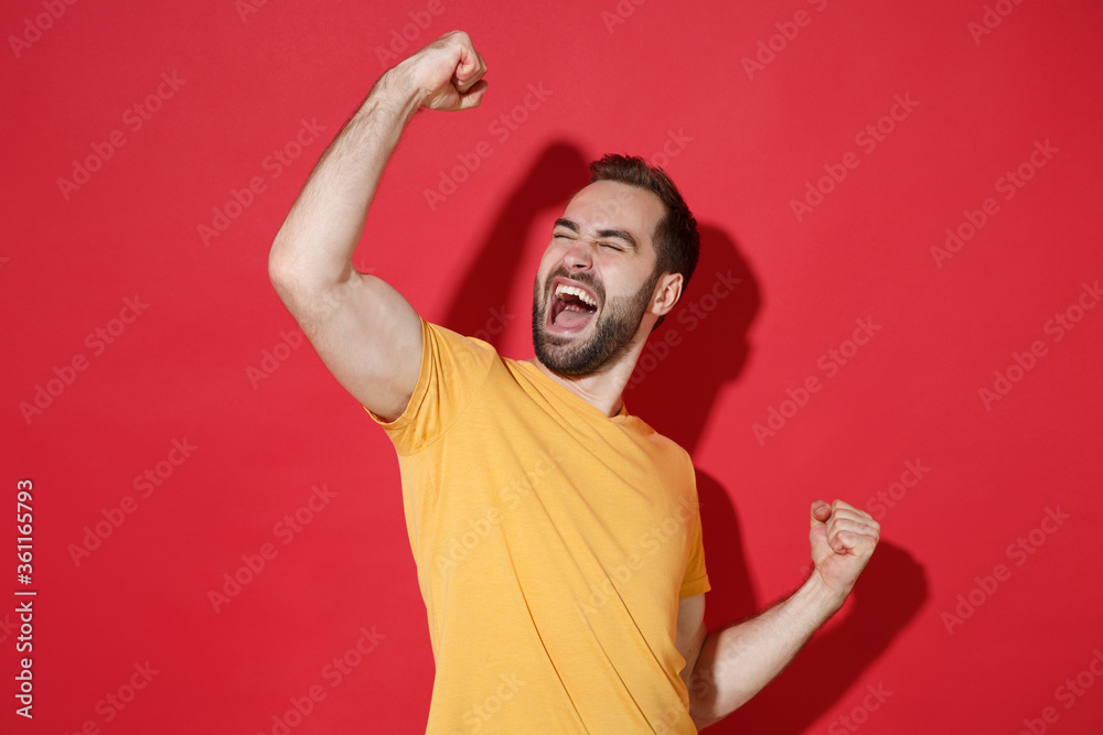 Joyful young bearded man guy in casual yellow t-shirt posing isolated on red background studio portrait. People sincere emotions lifestyle concept. Mock up copy space. Clenching fists like winner. Joyful young bearded man guy in casual yellow t-shirt posing isolated on red background studio portrait. People sincere emotions lifestyle concept. Mock up copy space. Clenching fists like winner.