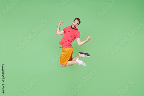 Side view of joyful young bearded man guy in casual red pink t-shirt posing isolated on green background studio portrait. People lifestyle concept. Mock up copy space. Jumping doing winner gesture.