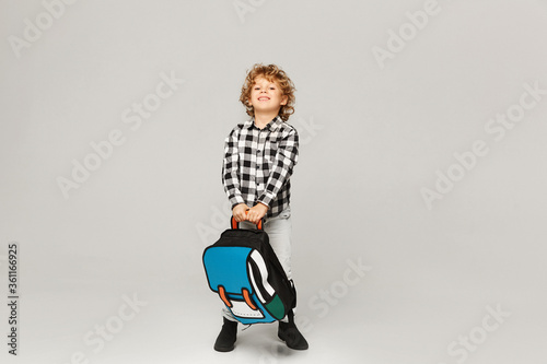 Back to school. A funny little boy from elementary school posing with a backpack over white background, isolated