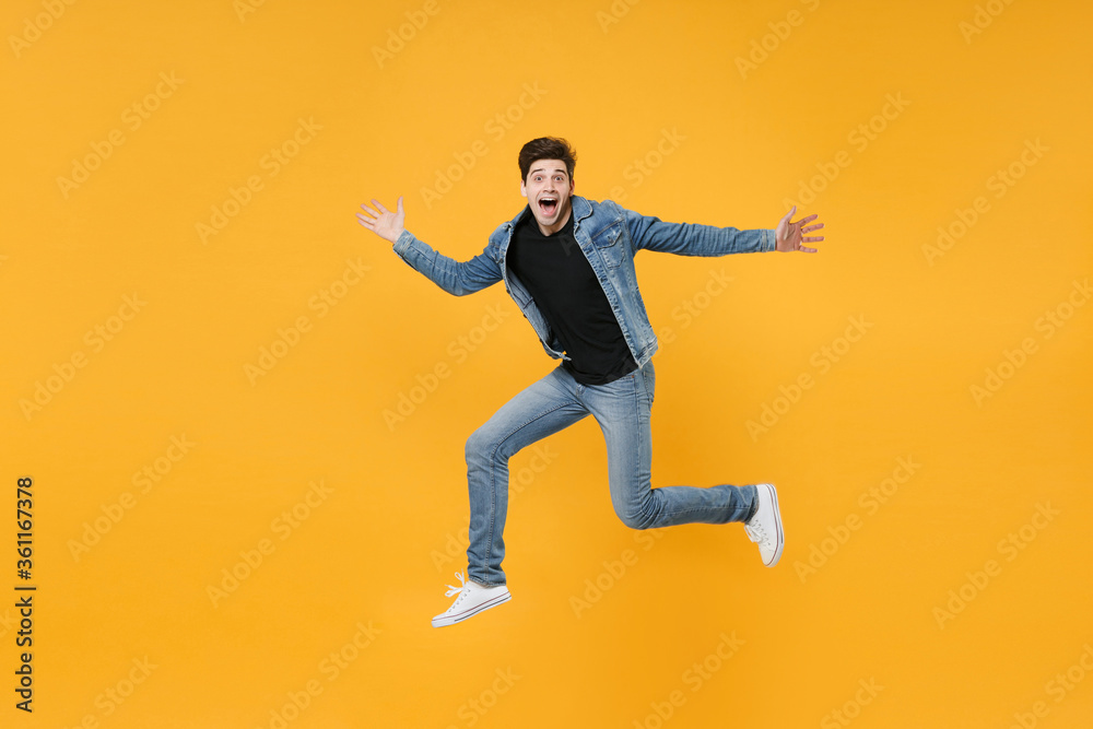 Surprised young man guy wearing casual denim clothes posing isolated on yellow background studio portrait. People sincere emotions lifestyle concept. Mock up copy space. Jumping, spreading hands legs.