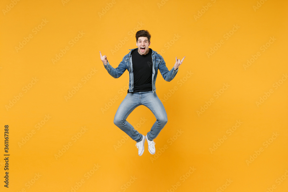 Screaming young man guy wearing casual denim clothes posing isolated on yellow wall background studio portrait. People lifestyle concept. Mock up copy space. Jumping, depicting heavy metal rock sign.