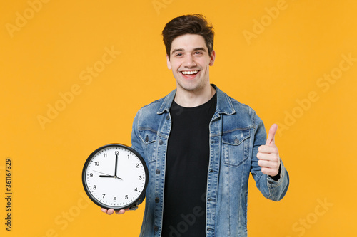 Foto Cheerful young man guy 20s in casual denim jacket posing isolated on yellow wall background studio portrait