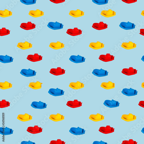 Seamless pattern of multi-colored plastic children’s boats on a light blue background