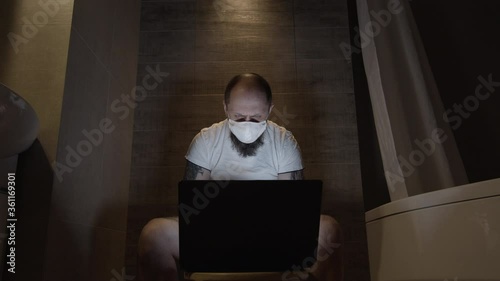 A man in a protective mask in the toilet works on a computer in quarantine