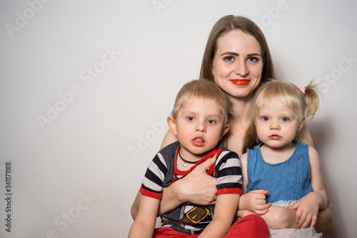 Happy family: young mother smiling and hugging her son and daughter on light background
