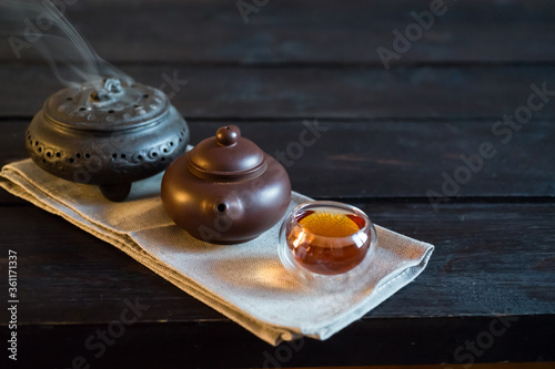 Teapot, incense and bowl with tea on light fabric and black wooden table