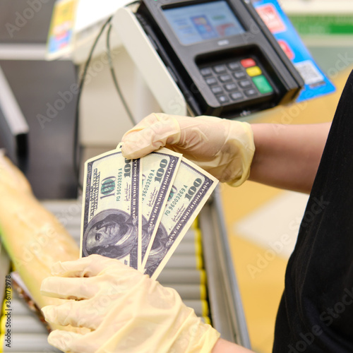 Hands in protective gloves count money at the cash register of the store. Dollars in the hands of a supermarket clerk