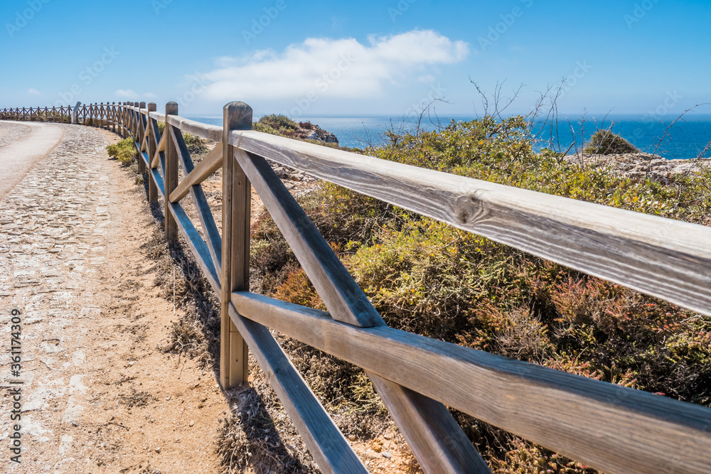 Perspective of wooden fence between sidewalk and cliff path by the sea, colorful and beautiful natural seascape image, Sagres PORTUGAL