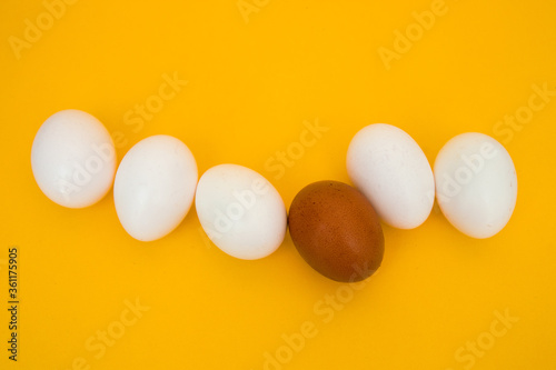 White eggs with a brown egg, as an accent on a yellow background