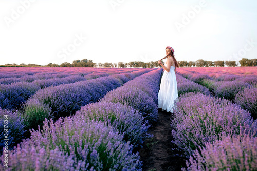 Beautiful woman in a white dress walks on a lavender field at sunset photo