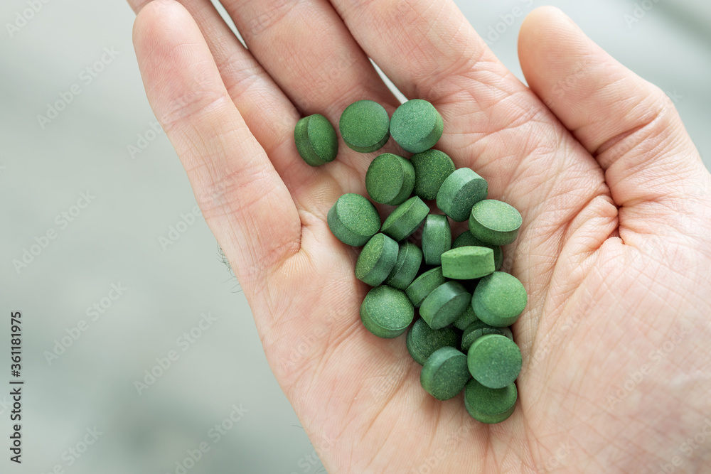 Hand with chlorella or spirulina tablets on grey background. Top view. Hand with chlorella or spirulina tablets on grey background. Top view.