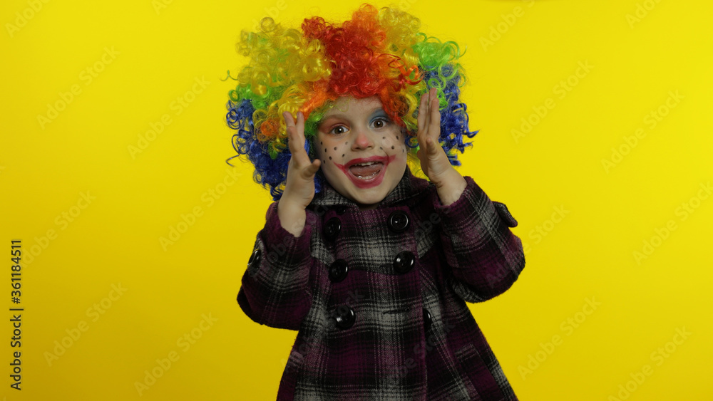 Little child girl clown in rainbow wig making silly faces. Having fun, smiling, dancing. Halloween Little child girl clown in rainbow wig making silly faces. Having fun, smiling, dancing. Halloween