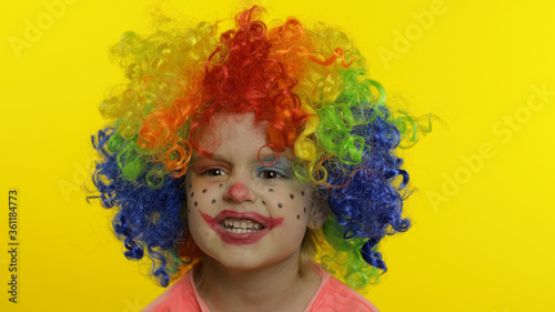 Little child girl clown in colorful wig making silly faces, having fun, smiling, dancing. Halloween