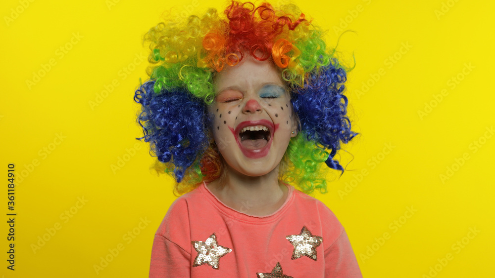 Little child girl clown in colorful wig making silly faces, having fun, smiling, dancing. Halloween Little child girl clown in colorful wig making silly faces, having fun, smiling, dancing. Halloween
