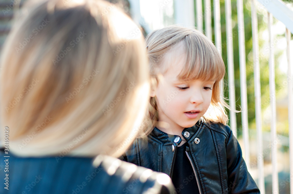 Beautiful little blonde girl, close-up portrait. Laughs and smiles at the camera. She plays with her mother in the same clothes of a family look: a red skirt , a black jacket, a t-shirt. Love for mom Beautiful little blonde girl, close-up portrait. Laughs and smiles at the camera. She plays with her mother in the same clothes of a family look: a red skirt , a black jacket, a t-shirt. Love for mom
