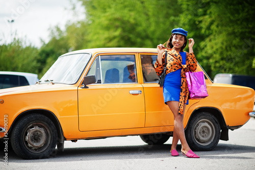 Beautiful african american lady with shopping bags standing near orange classic retro car. © AS Photo Family