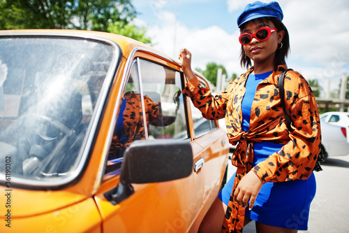 Beautiful african american lady with sunglasses standing near orange classic retro car.